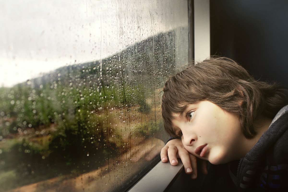 窓の外の雨を眺める男の子